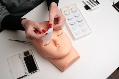 Kirpik uzatma teknikleri üzerinde çalışan bir güzellik mankeni. Kadın elleri göz altında pamuk bandı hazırlıyor. Kirpik yapmak için temel eğitim. Boşluğu kopyala