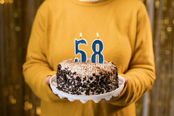 Woman holding a festive cake with number 58 candles while celebrating birthday party. Birthday holiday party people concept. Close-up view