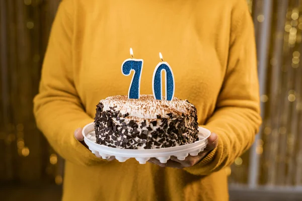 Woman holding a festive cake with number 70 candles while celebrating birthday party. Birthday holiday party people concept. Close-up view