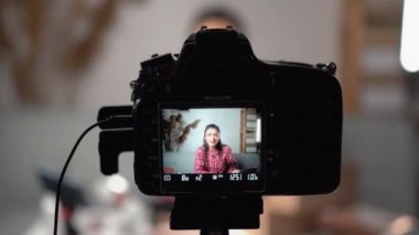 Kadın blogu için kozmetik hakkında bir video hazırlıyor. Dijital kamerayı tripoda kullanıyor. Kamera ekranında kozmetik ürünleri tutan blogcu kadını gösteriyor. Dijital kameraya odaklan. Boşluğu kopyala