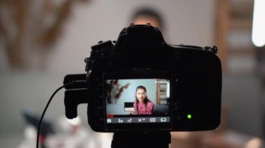 Genç bir kadın makyaj malzemesi tutmaktan bahsederken kendi stüdyosunda videosunu kaydediyor. Kadın güzellik blogu için video çekiyor. Boşluğu kopyala