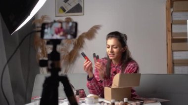 Kadın blogcu akıllı telefon kamerasında kozmetik makyaj ürünü gösteriyor. Vlog video canlı yayınını evde kaydediyor. Sosyal medya kavramı üzerinde iş çevrimiçi etkileyicisi.