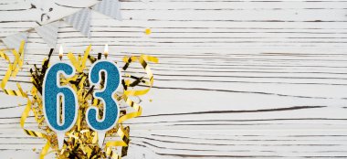 Beyaz ahşap arka planda 63 numaralı mavi kutlama mumu. Mutlu doğum günü mumları. Doğum günü, yıldönümü, önemli tarih, tatil kavramı. Uzayı kopyala Pankart