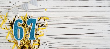 Beyaz ahşap arka planda 67 numaralı mavi kutlama mumu. Mutlu doğum günü mumları. Doğum günü, yıldönümü, önemli tarih, tatil kavramı. Uzayı kopyala Pankart