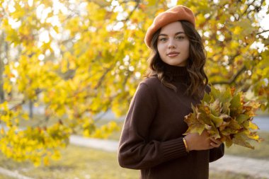 Sonbahar yaprakları yapraklarının önünde kameraya bakıp gülümseyen neşeli genç kadın portresi. Boşluğu kopyala