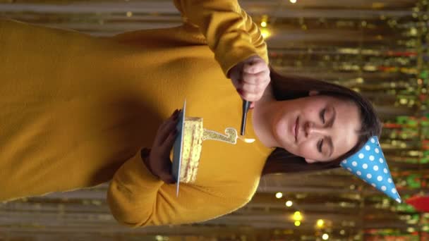 誕生日ケーキ照明のキャンドル番号7に喜びの若い女性は 黄金の背景の上に立って ホームパーティーでカメラを見て Pov 垂直ビデオ — ストック動画