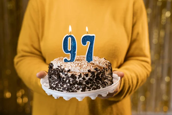 stock image Happy birthday. Woman holding fresh delicious birthday cake with burning candle number 97, close up. Celebration of birthday at home. Copy space