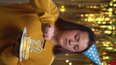 Doğum günü pastasının 22 numaralı mumunu çakmakla yakan kadın. Gülümseyen kız doğum günü pastası tutuyor ve partide kameraya bakıyor. Bakış açısı. Dikey video