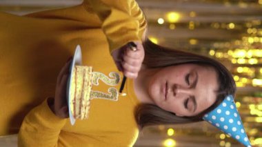 Doğum günü pastasında 27 numaralı mumları çakmakla yakan kadın. Gülümseyen kız doğum günü pastası tutuyor ve partide kameraya bakıyor. Bakış açısı. Dikey video