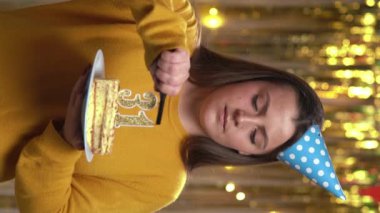 Doğum günü pastasında 32 numaralı mumları çakmakla yakan kadın. Gülümseyen kız doğum günü pastası tutuyor ve partide kameraya bakıyor. Bakış açısı. Dikey video