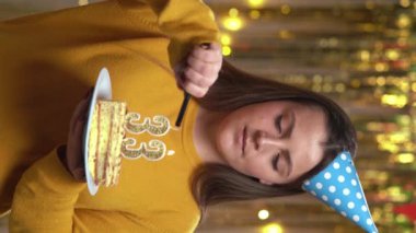 33 numaralı kadın pastadaki mumları çakmakla yakıyor. Gülümseyen kız doğum günü pastası tutuyor ve partide kameraya bakıyor. Bakış açısı. Dikey video