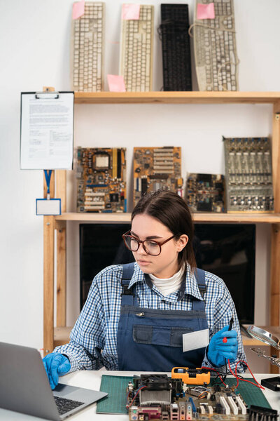 Small business-computer service. Computer technician testing motherboard at workshop using laptop. Copy space
