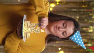 Ellerinde doğum günü pastası tutan güzel, mutlu, genç bir kadın. 52 numaralı altın mum çakmakla yanıyor. Doğum günü ve yıldönümü kutlaması kavramı. Bakış açısı. Dikey video