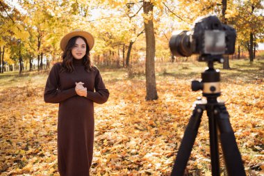 Young woman taking video for vlog on dslr camera. Female blogger influencer recording video content for blog in autumn park with yellow trees. Copy space