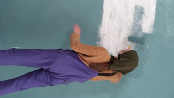 女人在家里的墙上涂上蓝色油漆 用油漆滚筒 背对着相机 垂直录像 — 图库视频影像