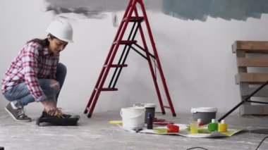 Boyacı kadın evin duvarını boya rulosu ve gri boyayla boyuyor. Evdeki oda tadilatı. Boşluğu kopyala