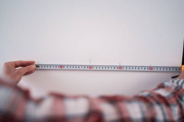 Ev tadilatı için mezura kullanan kadın işçi. Beyaz duvarda önlem alan bir kadın. Ev tadilatı sırasında inşaat bandıyla duvarı ölçer. Boşluğu kopyala