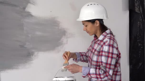 戴防护头盔的妇女使用漆刷 墙上涂灰色油漆 画一个墙的概念 靠近点 — 图库视频影像