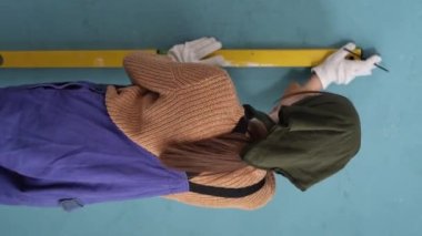Duvara çarpıp iz bırakmak için ruh seviyesini kullanan bir kadın. Ev yenileme konsepti. Duvar seviyesini kontrol ediyor. Dikey video