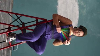 Boyacı kadın, yarı boyanmış duvarda mavi bir palet gösteriyor, kırmızı merdivende oturuyor. Ev, taşınma, dekorasyon, yenileme ve duvar boyama konsepti. Dikey video
