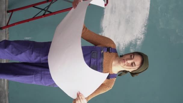 家の改造や家のインテリアの再設計 紙の青写真を持つかわいい女の子 フラットの改修プロジェクトを勉強若い白人女性 垂直ビデオ — ストック動画