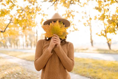 Sonbaharda parkta elinde yapraklarla bekleyen güzel, mutlu genç bir kadın. Sonbaharda açık havada neşeli bir kız. Boşluğu kopyala