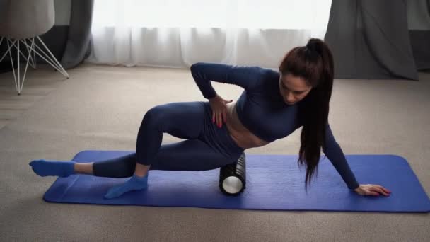 身穿蓝色西服的女运动员在地板上做筋膜运动 用按摩泡沫滚筒作为工具来缓解背部的紧张和肌肉疼痛 复制空间 — 图库视频影像