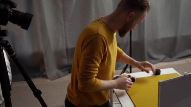 Erkek fotoğrafçı, tripodun üzerinde kamera kullanarak güzellik ürünleri hazırlıyor. Fotoğrafçı ev stüdyosunda fotoğraf çekmeye çalışıyor. Boşluğu kopyala
