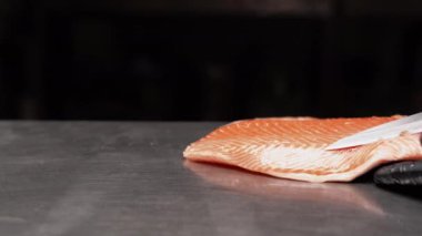 Şefin elleri kesim masasında taze somon hazırlarken Japon aşçı somon balığı için çiğ balık keserken bıçak kullanıyor. Somon filetosu dilimlemek için