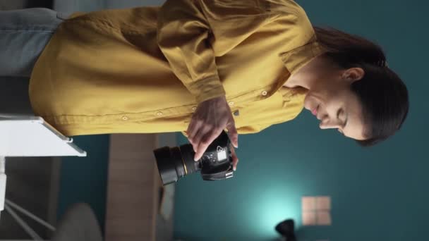 自宅のオフィスでスラーカメラを持っている美しい若い写真家 新しいプロジェクトで働くクリエイティブな女性フリーランス 垂直ビデオ — ストック動画