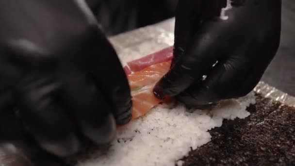 黒い手袋でシェフの手を閉じて レストランで日本の寿司ロールの準備 暗い背景 — ストック動画