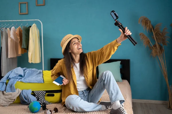 stock image Social media vlogging concept. Young travel vlogger recording video content on smartphone, sitting on bed near the suitcase, speaking to her blog about journey. Copy space