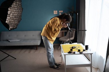Ev stüdyosundaki masada güzellik ürünleri çeken kadın fotoğrafçı fotoğraf çekmeye çalışıyor. Yaratıcı genç fotoğrafçı. Güzellik blogu kariyer kavramı