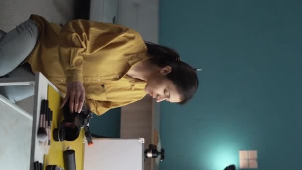 自宅のスタジオでテーブルの上で美容製品を撮影する女性写真家 垂直ビデオ — ストック動画