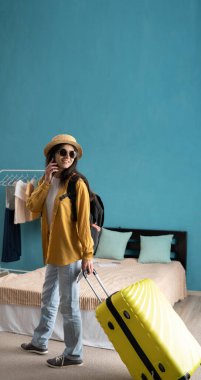 Bavullu Millennial güzeli kadın tatile çıkıyor. Bayan gezgin otel odasından telefonla konuşuyor. Yaz tatili kavramı