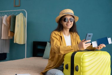 Teknoloji ve seyahat konsepti. Şapkalı İspanyol kadın elinde pasaport ve uçak biletleriyle havaalanına gitmek için taksi beklerken akıllı telefon kullanıyor. Boşluğu kopyala