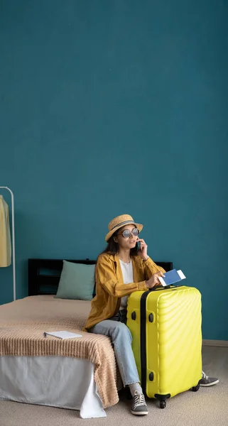 stock image Woman traveler talking on mobile phone, sitting on bed at suitcase calling a taxi calls, waiting for transport to the airport, she sits with baggage indoor flat, ready travel. Banner. Copy space