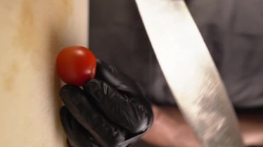 Bıçaklı erkek eller tahta kesme tahtasıyla küçük domatesler kesiyor. Yemek pişirmek için çevre dostu ürünler kavramı. Dikey video