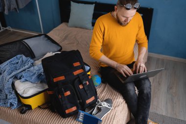 Genç sakallı adam dizüstü bilgisayarla tatil seyahati planlıyor, internetten bilet ayırtıyor ya da otel odası ayırtıyor, yurt dışı seyahatine hazırlanıyor. Boşluğu kopyala