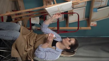 Sanat stüdyosunda çalışan yaratıcı genç bir kadın. Modern bir soyut resim üzerinde çalışan yetenekli bir kadın sanatçı. Sanat, yaratıcılık ve insan konsepti. Dikey video