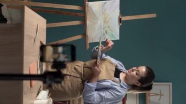 Sanat ressamı yaşıyor. Kadın sanatçı, atölyesinde akıllı telefon kullanarak resim hakkında video dersi veriyor. Dikey video