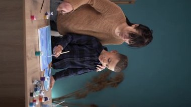 Bir okul çocuğu olan genç bir anne evde akriliklerle vakit geçirir ve resim yapar. İlham, eğitim ve sanat konsepti. dikey video. Boşluğu kopyala.