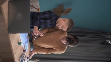 Mutlu bir aile. Anne ve oğlu evdeki tuvalde günlük kıyafetlerle akrilik boya yapmayı internetten öğreniyorlar. Bir dizüstü bilgisayar kullanarak. İlham, eğitim ve sanat konsepti. Dikey görünüm. Boşluğu kopyala.