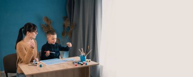 Genç ve güzel bir kadın, okul oğluna tuvale yağlı boya ile resim yapmayı öğretiyor. Bir kadın çocuğuyla vakit geçirir. Pankart. Boşluğu kopyala.