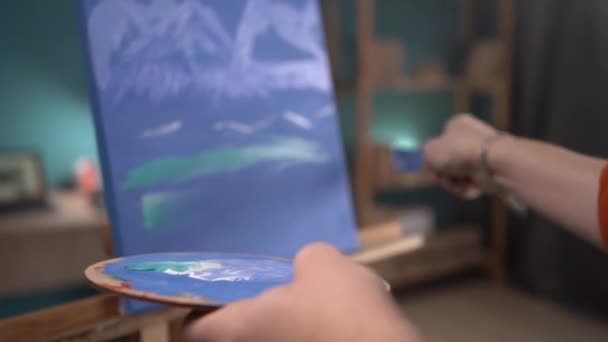 才能ある若い芸術家がキャンバスに絵を描く ブラシで手にパレットを持ちブラシでキャンバスに線を描く クローズアップ 選択的焦点 絵画の概念 趣味としての仕事 — ストック動画