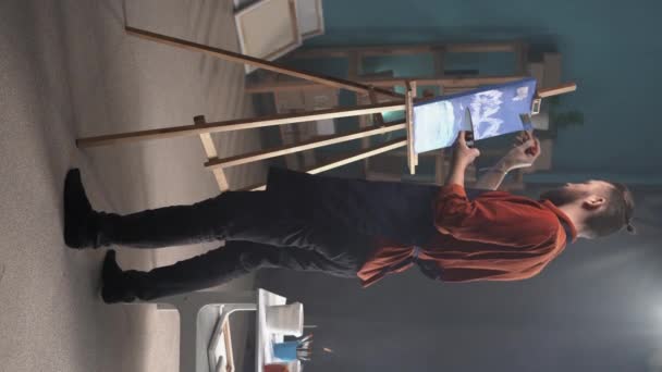 聚精会神的高加索胡子男人在围裙上画了一幅画在画布上的家庭工作室 后视镜 创意和艺术概念 垂直视频 — 图库视频影像