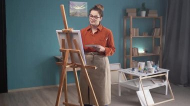 Gözlüklü güzel bir kadın tuvale resim yapıyor. Hobi ve eğlence konsepti. Boşluğu kopyala.