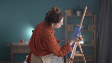 Genç kadın ressam ev manzarasında yaratıcı tablolar çiziyor. Hobi ve tatil konsepti. Boşluğu kopyala.