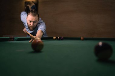 Sıradan giysiler içinde bilardo oynayan beyaz bir adam. Topa vurmaya hazırlanıyorum. Top fotokopi alanının kenarından çekim.
