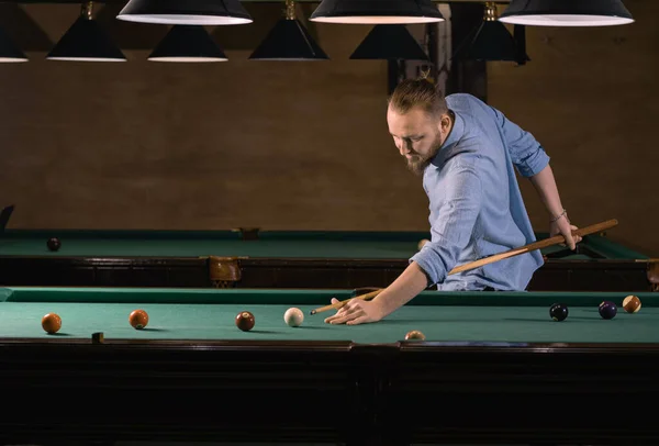 stock image concentrated caucasian man in casual clothes playing billiards. getting ready to hit the ball. banner. copy space.